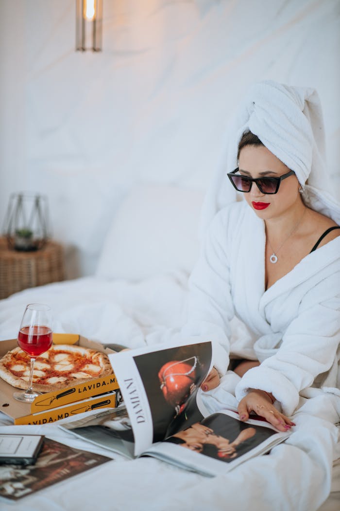 about-02 Woman in robe enjoying pizza and magazines in bed for a relaxed morning moment.